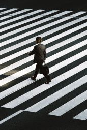 A man in a suit with a black bag walks in a crosswalk. Processes of Organizational growth may lead to founders stepping down. CDS fundraising. 