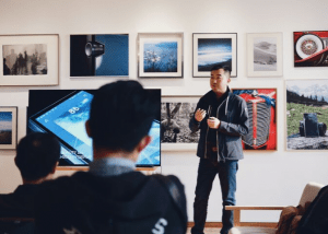 A man gives a lecture in a gallery with two businessmen listening on. Express Yourself like this lecturer. Custom Development Solutions. 