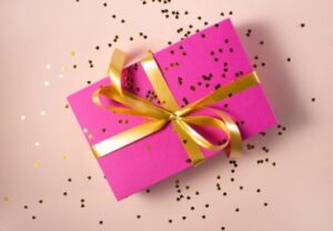 A pink wrapped gift box with gold ribbon covered with gold hearts. CDS Inc. 