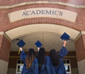 A set of three graduates in blue gowns celebrate in front of a brick academics building. Without building a external Constituency Universities will be in trouble. Custom Development Solutions. 