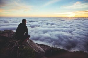 A man on a mountaintop looking at a sea of clouds below. What is he envisioning? Custom Development Solutions.