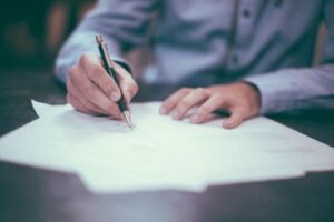 A man writes on a page siting on a dark brown desk, taking notes on how to build a strong solicitation team from Custom Development Solutions.