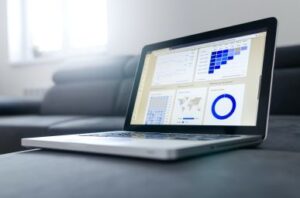 A laptop showing blue charts on a grey chair near a window. A succeful capital campaign means keeping an eye on things. Custom Development Solutions.