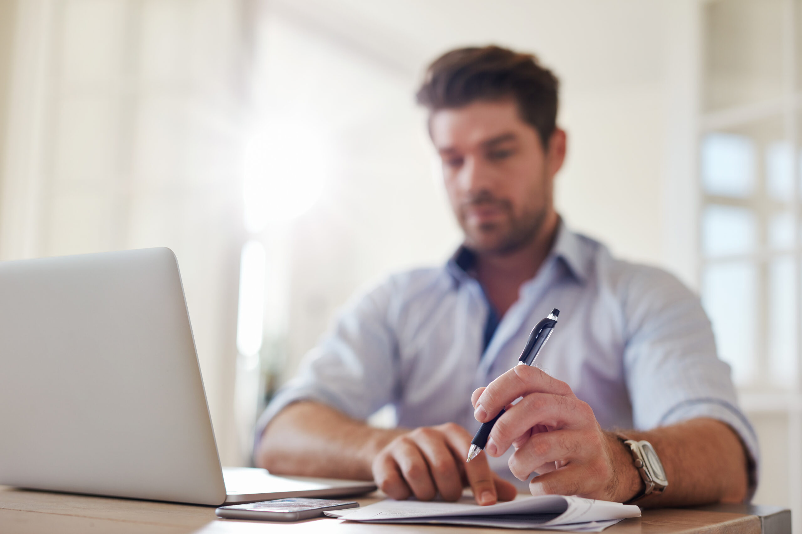 Shot of young businessman at home office with laptop and taking notes on a campaign leadership gift phase from Custom Development Solutions. 