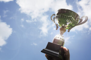 Someone holding a trophy up against a blue sky with clouds. Why try your best? Because you can!