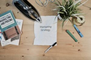 An image of a wooden desk with various cluter with a piece of paper with Marketing Strategy on it in the center. Custom Development Solutions.