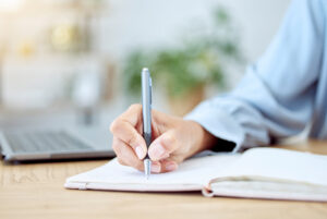 Woman taking notes on a case for support in a notebook beside her laptop.