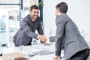 Two men shake hands in an office, representing a sponsorship agreement deal being made.