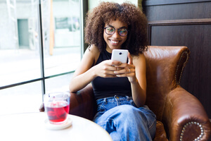 A young alumna sits in a chair and smiles at a text on her phone.